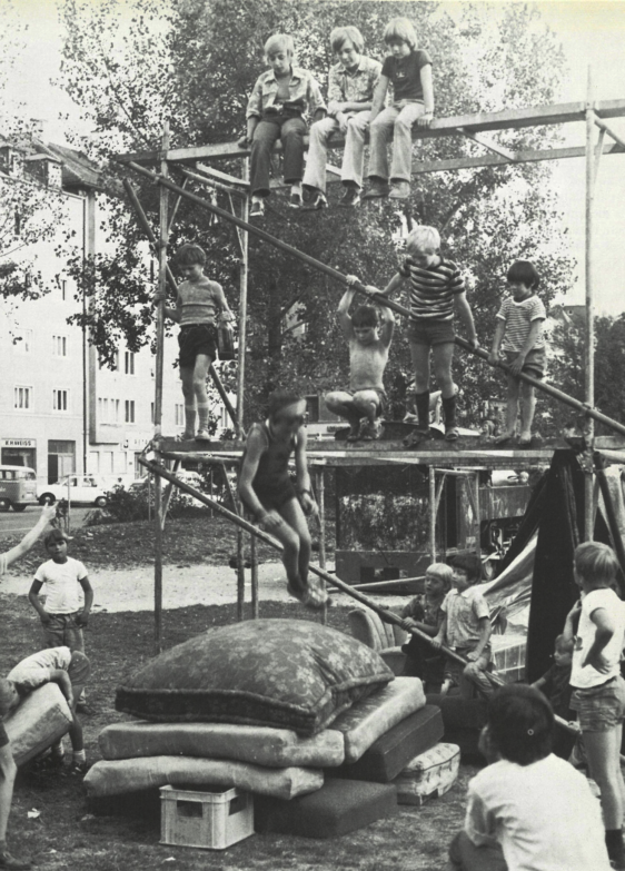 Kinder spielen auf einem Gerüst; im Vordergrund ein Stapel Matten.